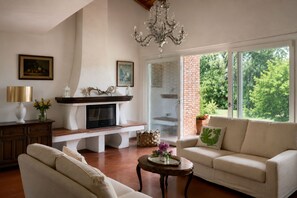 Een woonkamer met een open haard, bank en een groot raam met uitzicht op groen.