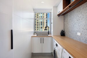 Eine kompakte Küche mit integriertem Waschtrockner, einem Fenster mit Blick auf ein Hochhaus und einer gefliesten Spritzschutzwand.