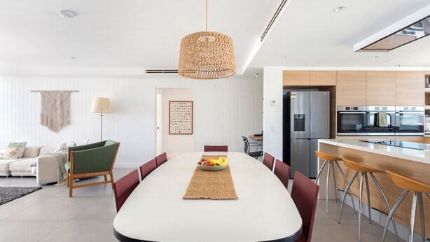 Een moderne keuken met roestvrijstalen apparatuur, een eethoek met een witte tafel, en een zithoek met een groene stoel en een macramé wanddecoratie.