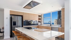 Een moderne keuken met een centraal eiland, roestvrijstalen apparatuur en stadszicht door grote ramen.