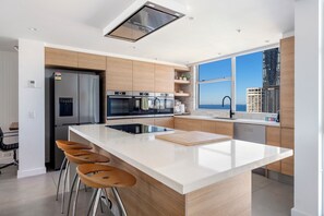 Eine moderne Küche mit Kochinsel, Edelstahlgeräten und Blick auf die Stadt durch große Fenster.