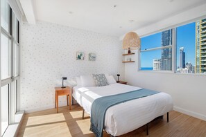 A modern bedroom with a large bed, two bedside tables, a city view, and a polka dot wallpaper. - Wake to stunning ocean views from this modern Surfers Paradise apartment. Enjoy a private balcony, resort pool, spa, kids playground, and tennis court, with the beach, Cavill Avenue, shopping and dining all just a short walk away. (Surfers Paradise)