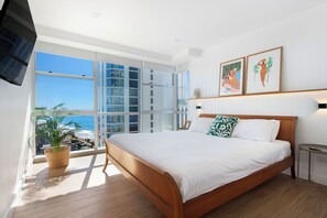 Ein Schlafzimmer mit einem großen Bett, Blick aufs Meer und zwei gerahmten Kunstwerken an der Wand.