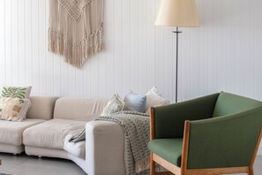 Ein Wohnzimmer mit einer Couch, einem grünen Sessel, einer Stehlampe und einer Wandweberei aus Makramee.