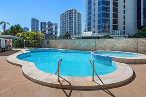 A swimming pool with two ladders, surrounded by a stone wall, with tall buildings in the background.