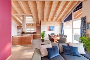A modern interior with a wooden ceiling, a dining area with a table and chairs, a kitchen with built-in appliances, and a large window with curtains. - Powder Snow Loft - by Zermatt Apartment Rentals : Matterhorn Views, sleeps 6-7 (zermatt)