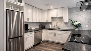 Una cucina moderna con mobili bianchi, elettrodomestici in acciaio inossidabile e una parete di fondo in marmo.