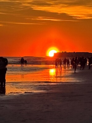 Een zonsondergang boven een strand, met mensen en paarden.