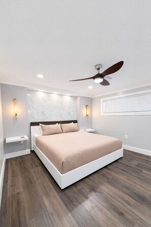Ein modernes Schlafzimmer mit einem großen Bett, einem Deckenventilator und Wandleuchten.