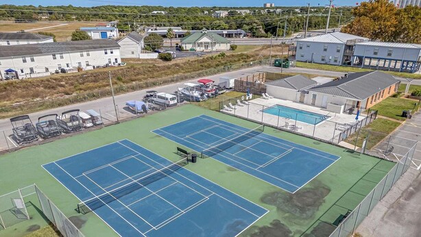 Un campo da tennis con una rete, circondato da una recinzione e adiacente a un edificio con piscina.