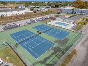 A tennis court with a net, surrounded by a fence, and adjacent to a building with a pool. - LUXURY 1-bedroom condo in Destin (Destin)