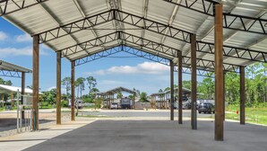 A covered parking area with a metal roof and concrete floor, surrounded by trees and buildings. - RV Site, Full Hookup, Flo's RV Home (Port St. Joe)
