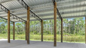 A large open space with a metal roof supported by wooden beams, overlooking a body of water and a forested area. - RV Site, Full Hookup, Flo's RV Home (Port St. Joe)