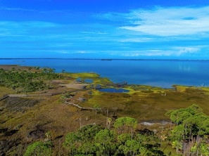 A coastal landscape with a wooden boardwalk, grassy areas, and a calm body of water.