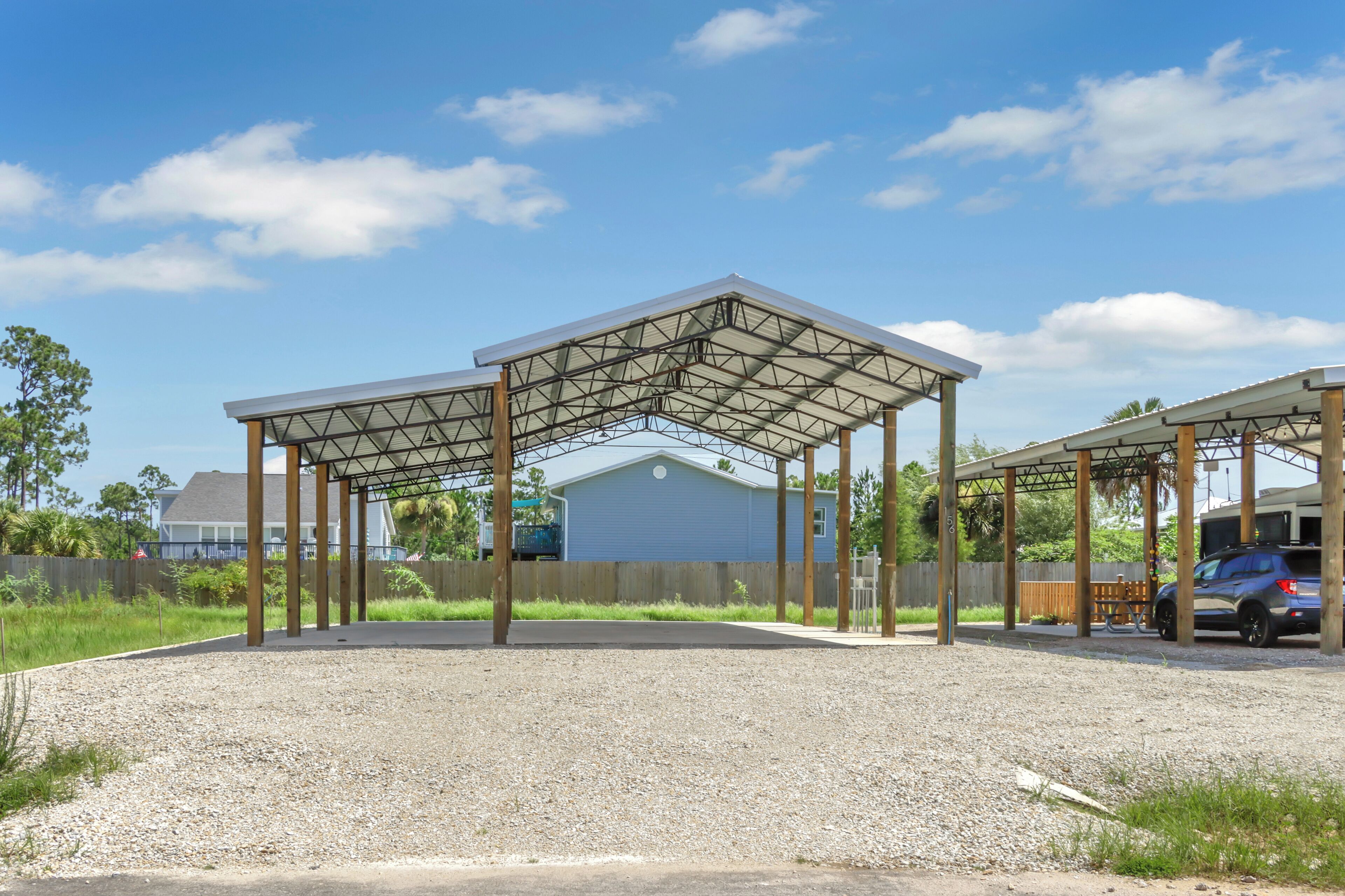 A covered outdoor area with a gravel ground, wooden posts, and a metal roof structure.
