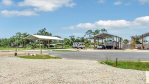 A campground with covered structures, RVs, and a gravel parking area. - RV Site, Full Hookup, Flo's RV Home (Port St. Joe)