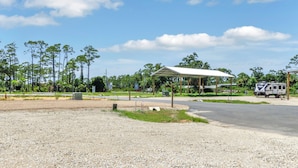 A gravel parking area with a covered pavilion and a recreational vehicle. - RV Site, Full Hookup, Flo's RV Home (Port St. Joe)