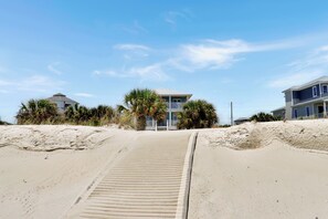 Une plage avec un sentier sablonneux menant à un bâtiment doté d’un balcon.