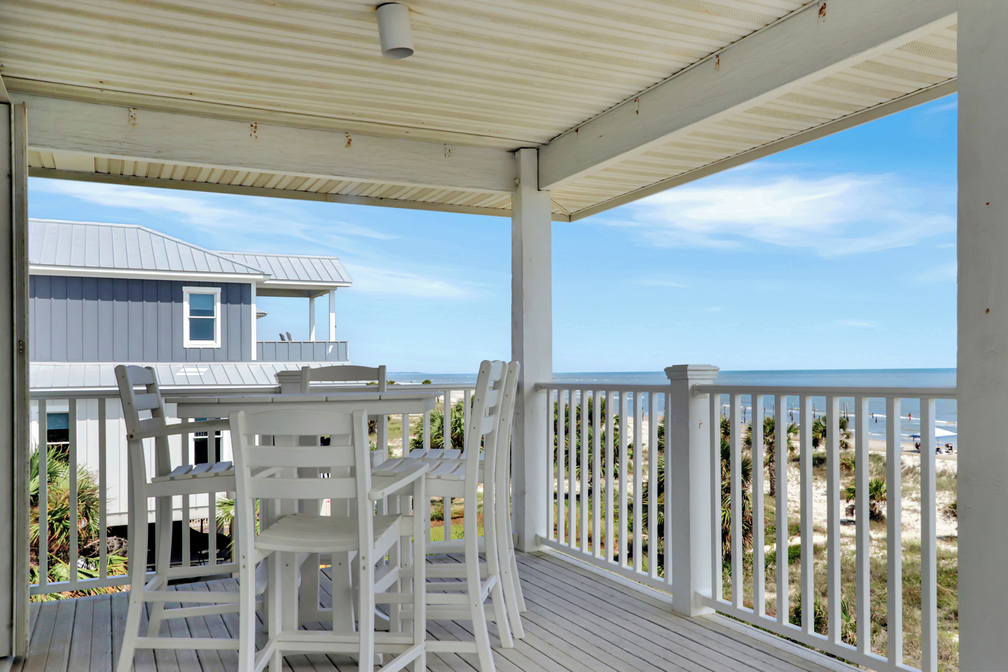 Un espace extérieur abrité, doté d’une table et de chaises, qui offre une vue sur une plage et une maison.