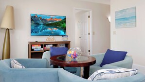 A living room with a flat-screen TV on the wall, a glass coffee table with a decorative item, and two blue sofas. - Beachfront Home | Hot tub | Pet Friendly | Sea Palms (Indian Pass)