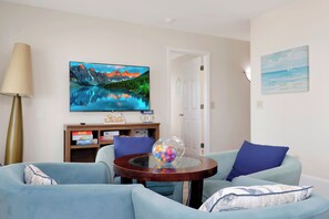 A living room with a flat-screen TV on the wall, a glass coffee table with a decorative item, and two blue sofas. - Beachfront Home | Hot tub | Pet Friendly | Sea Palms (Indian Pass)