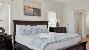 A bedroom with a bed, a nightstand, a lamp, a painting, and a door. - Beachfront Home | Hot tub | Pet Friendly | Sea Palms (Indian Pass)
