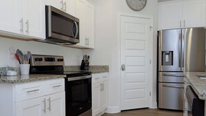 A kitchen with white cabinets, a microwave, a stove, a refrigerator, and a clock on the wall. - 🌊Seaside Escape | Windmark Beach | Pool + Beach Access (WindMark Beach)