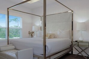 A four-poster canopy bed with white bedding, a bedside table with a lamp, and a view of the outdoors through a window with blinds. - 🌊Seaside Escape | Windmark Beach | Pool + Beach Access (WindMark Beach)