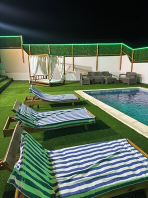 A pool area with lounge chairs and a bed.