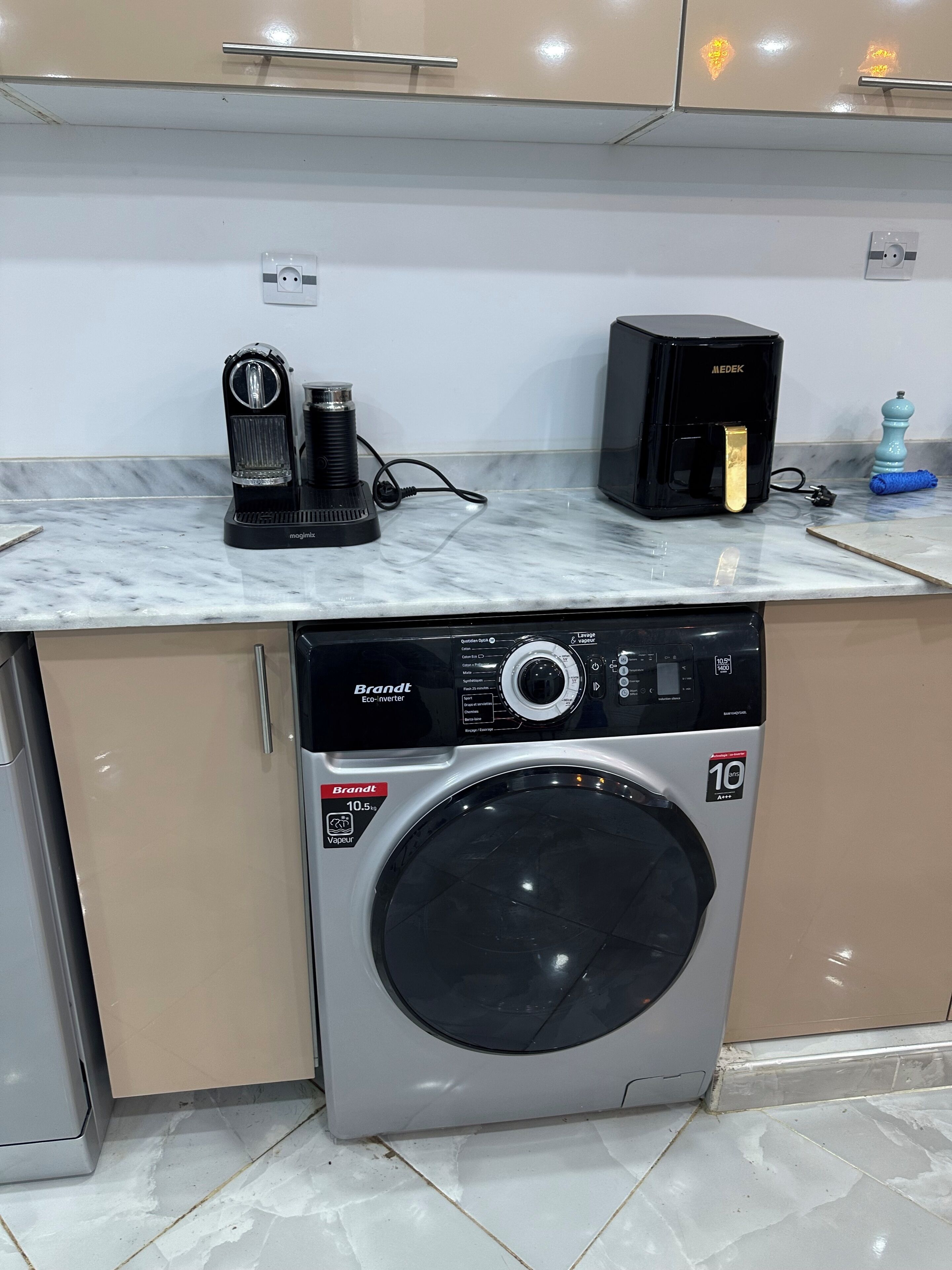Une cuisine compacte équipée d’un lave-linge encastré, d’une machine à café et d’un four à micro-ondes posé sur le plan de travail.