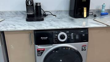 Une cuisine compacte équipée d’un lave-linge encastré, d’une machine à café et d’un four à micro-ondes posé sur le plan de travail.