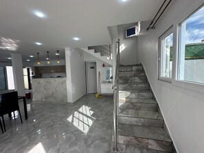 A modern interior with a marble staircase, a kitchen area, and a dining space.