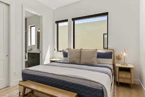 A bedroom with a bed, bedside tables, a bench, and a large window. - Lagoon Landing 7 Bedroom Home (St. George)
