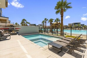 A swimming pool with lounge chairs and a fire pit, surrounded by palm trees and modern buildings. - Lagoon Landing 7 Bedroom Home (St. George)