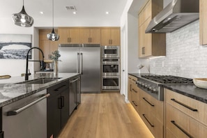 A modern kitchen with stainless steel appliances, wooden cabinets, and a marble countertop. - Lagoon Landing 7 Bedroom Home (St. George)