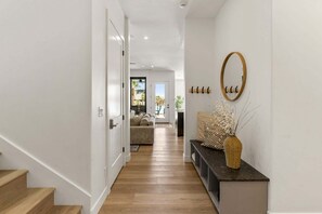 A hallway with a wooden staircase, a bench with a vase, and a view into a living area with a pool. - Lagoon Landing 7 Bedroom Home (St. George)