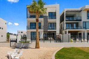 A modern multi-story building with balconies, a palm tree, and outdoor seating. - Lagoon Landing 7 Bedroom Home (St. George)