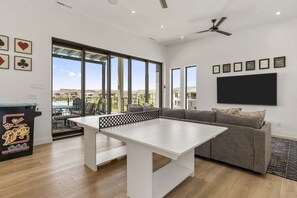 A modern living room with a pool table, a sofa, and a TV mounted on the wall. - Lagoon Landing 7 Bedroom Home (St. George)