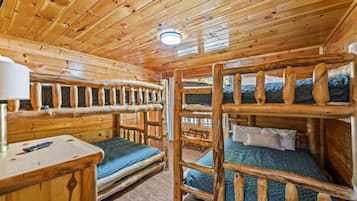 Interior de cabana com beliches, teto de madeira e uma mesinha com luminária.