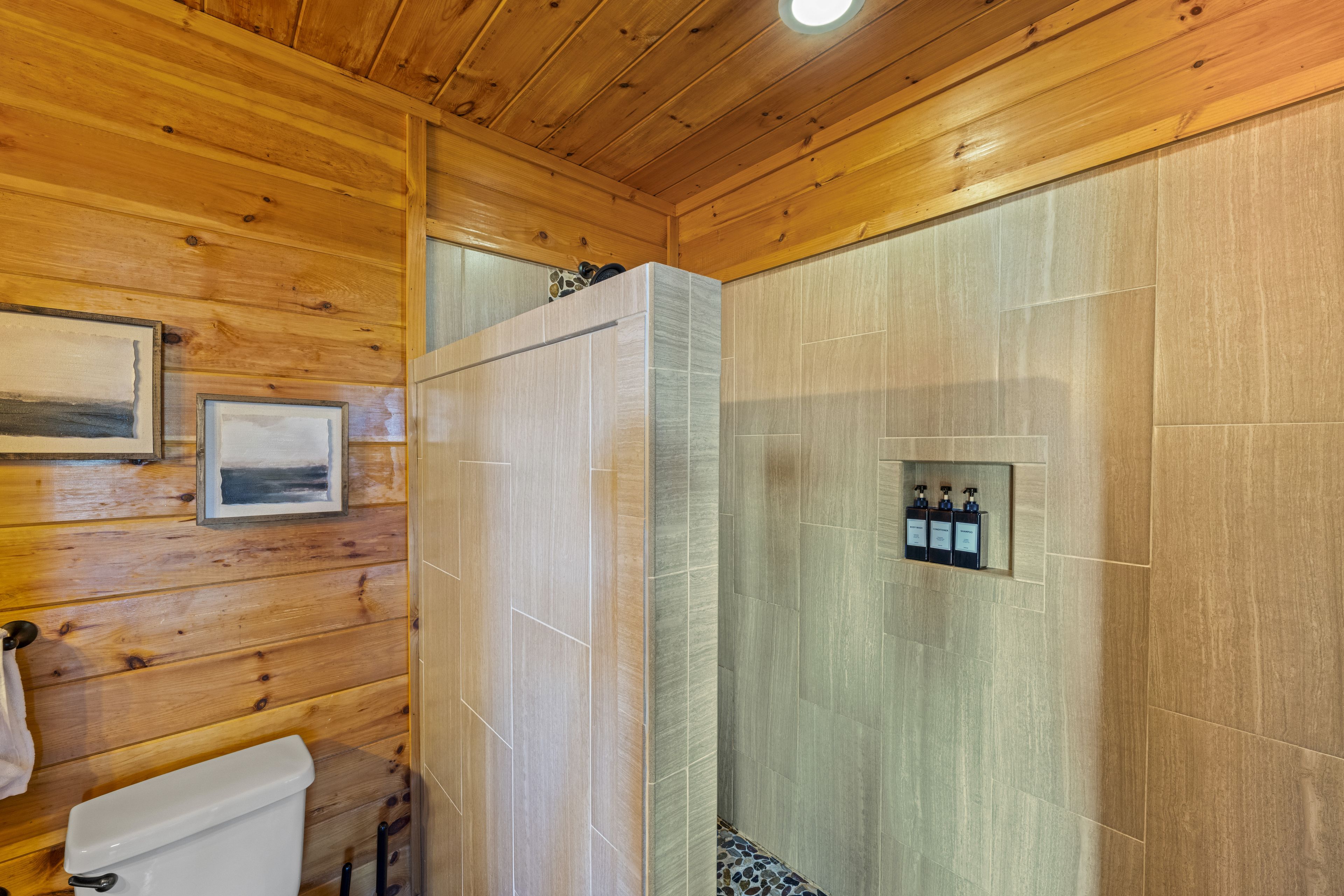 Baño de cabaña de madera con ducha, inodoro y fotografías enmarcadas en la pared.