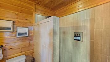Baño de cabaña de madera con ducha, inodoro y fotografías enmarcadas en la pared.