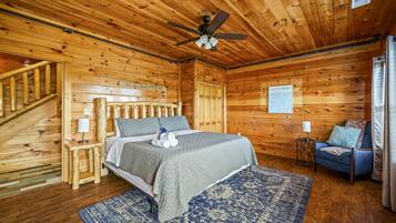 Un dormitorio de cabaña de madera con cama, una silla, una mesita de noche, un ventilador de techo y una escalera.