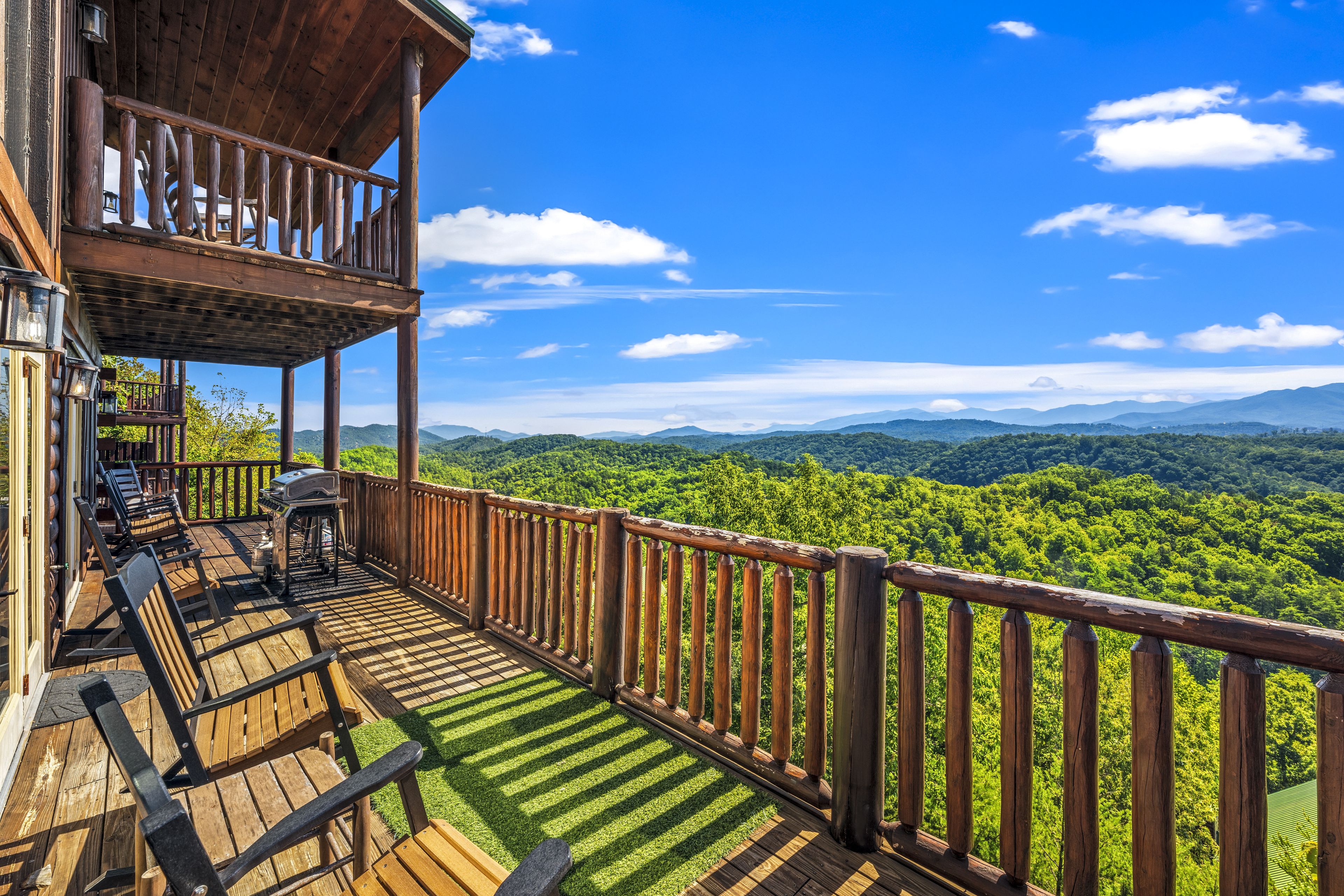 A wooden deck with outdoor furniture and a grill, overlooking a forested landscape.