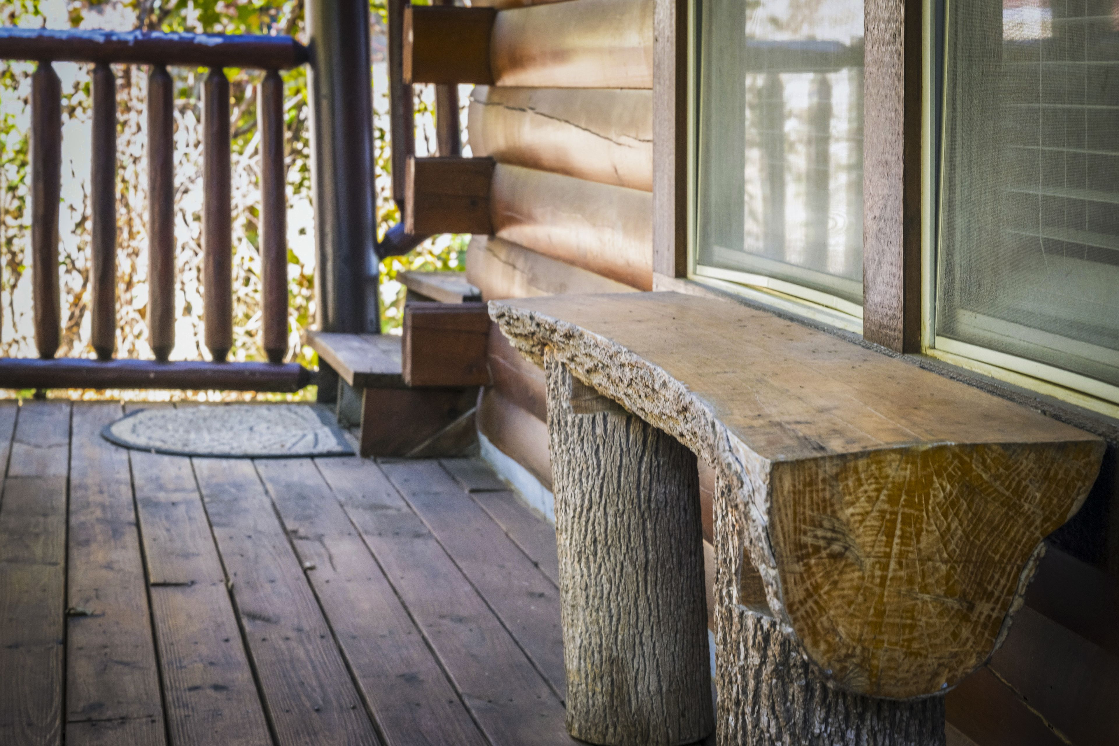 Una terraza de madera con un banco y un tocón de árbol usado como mesa.