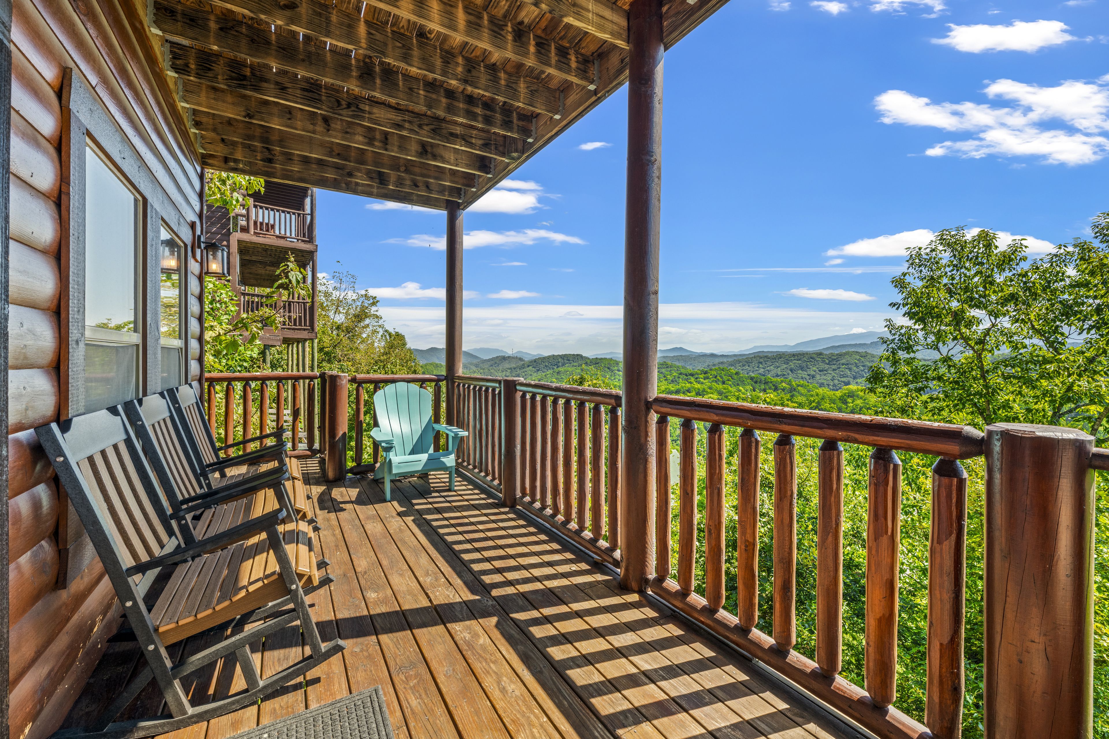 Una terraza de madera con vistas a un paisaje montañoso, una silla Adirondack azul y una barandilla de madera.