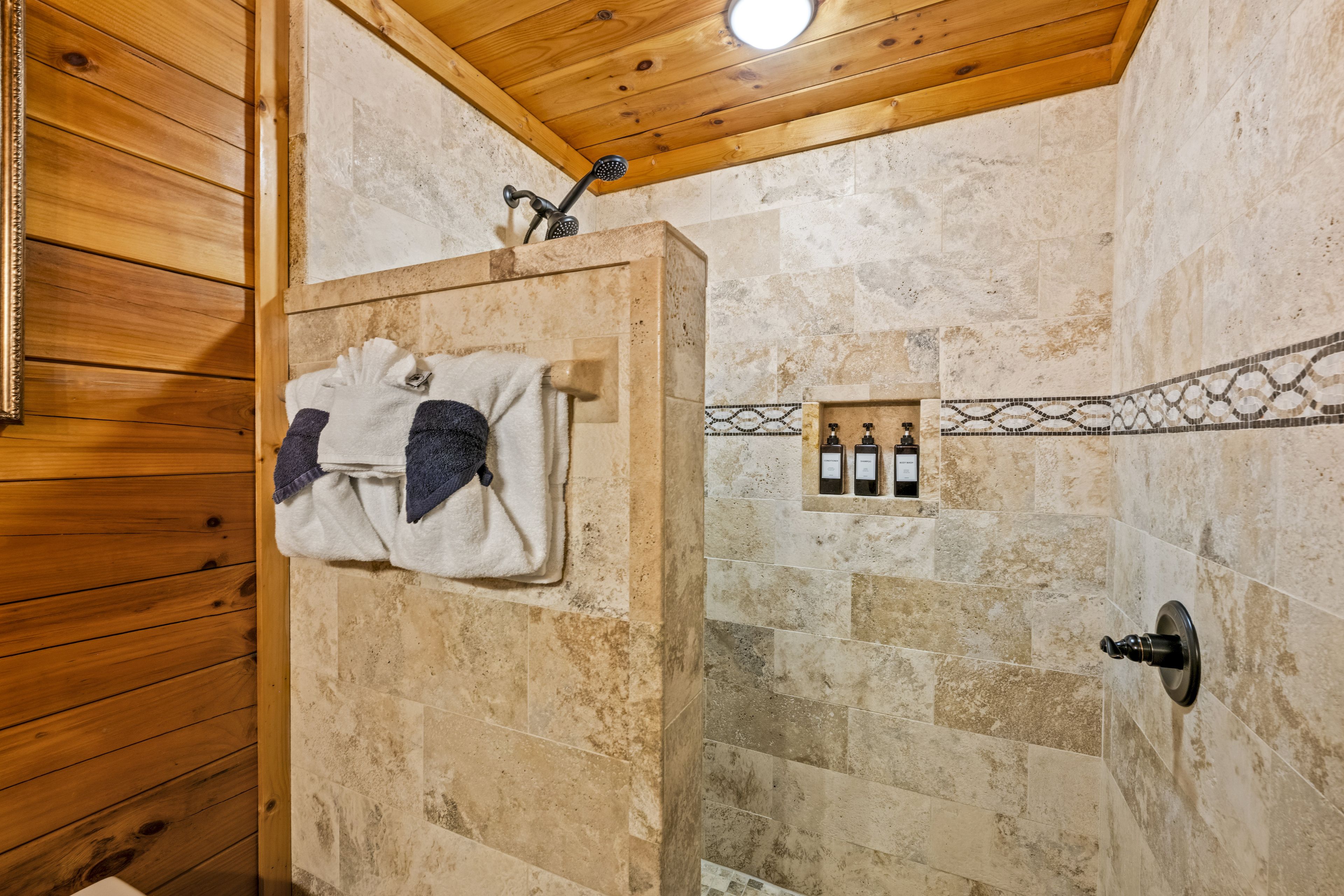 Zona de ducha con techo de madera, paredes de piedra y un perchero con toallas.