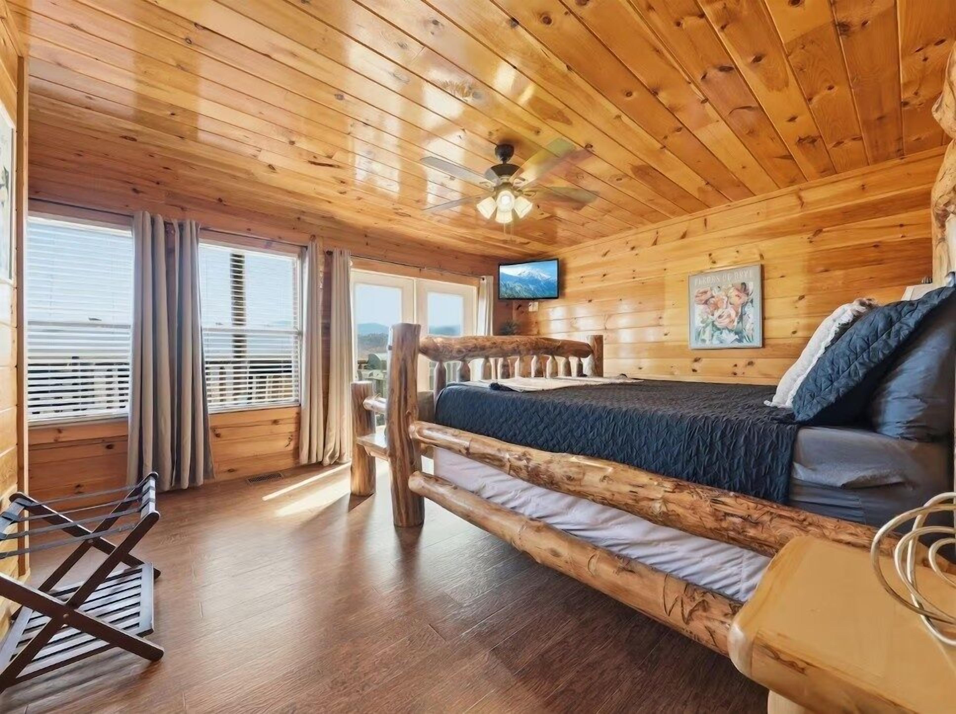 Una habitación tipo cabaña de madera con una cama, televisión y vista a las montañas.