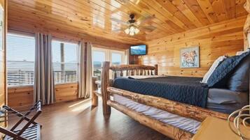 Una habitación tipo cabaña de madera con una cama, televisión y vista a las montañas.