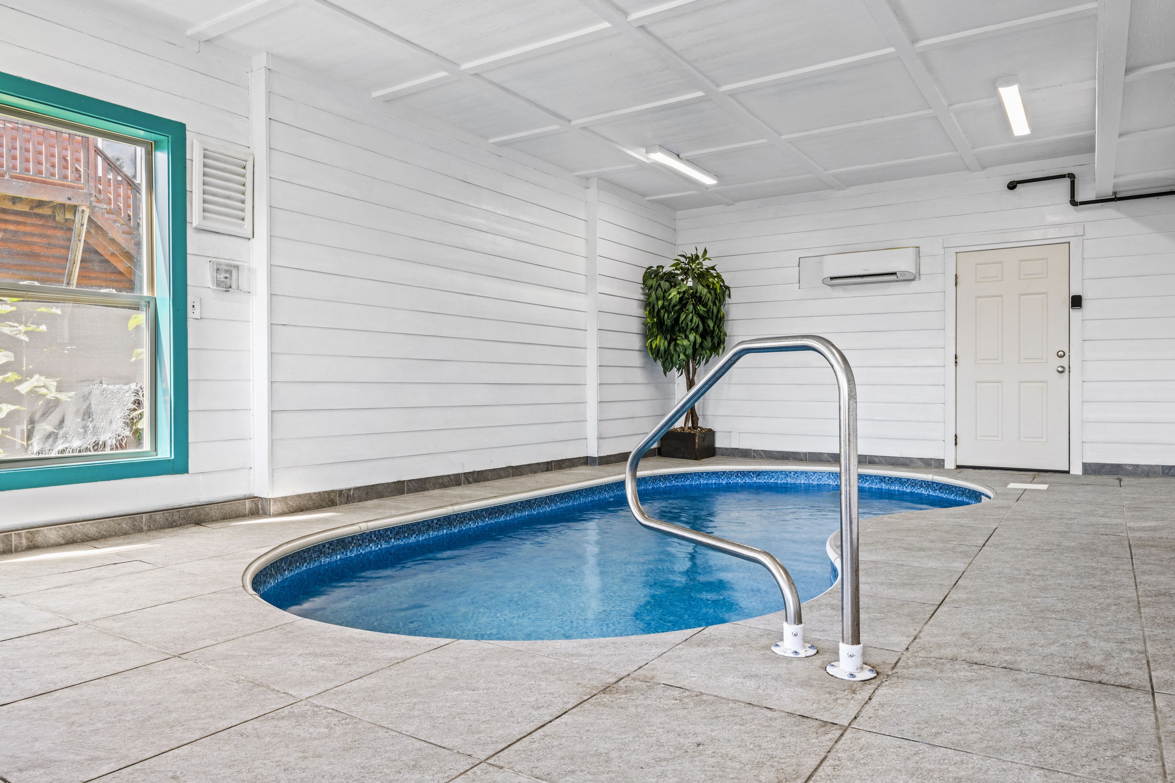 Una piscina con una escalera de metal, rodeada de paredes blancas y un suelo de baldosas.