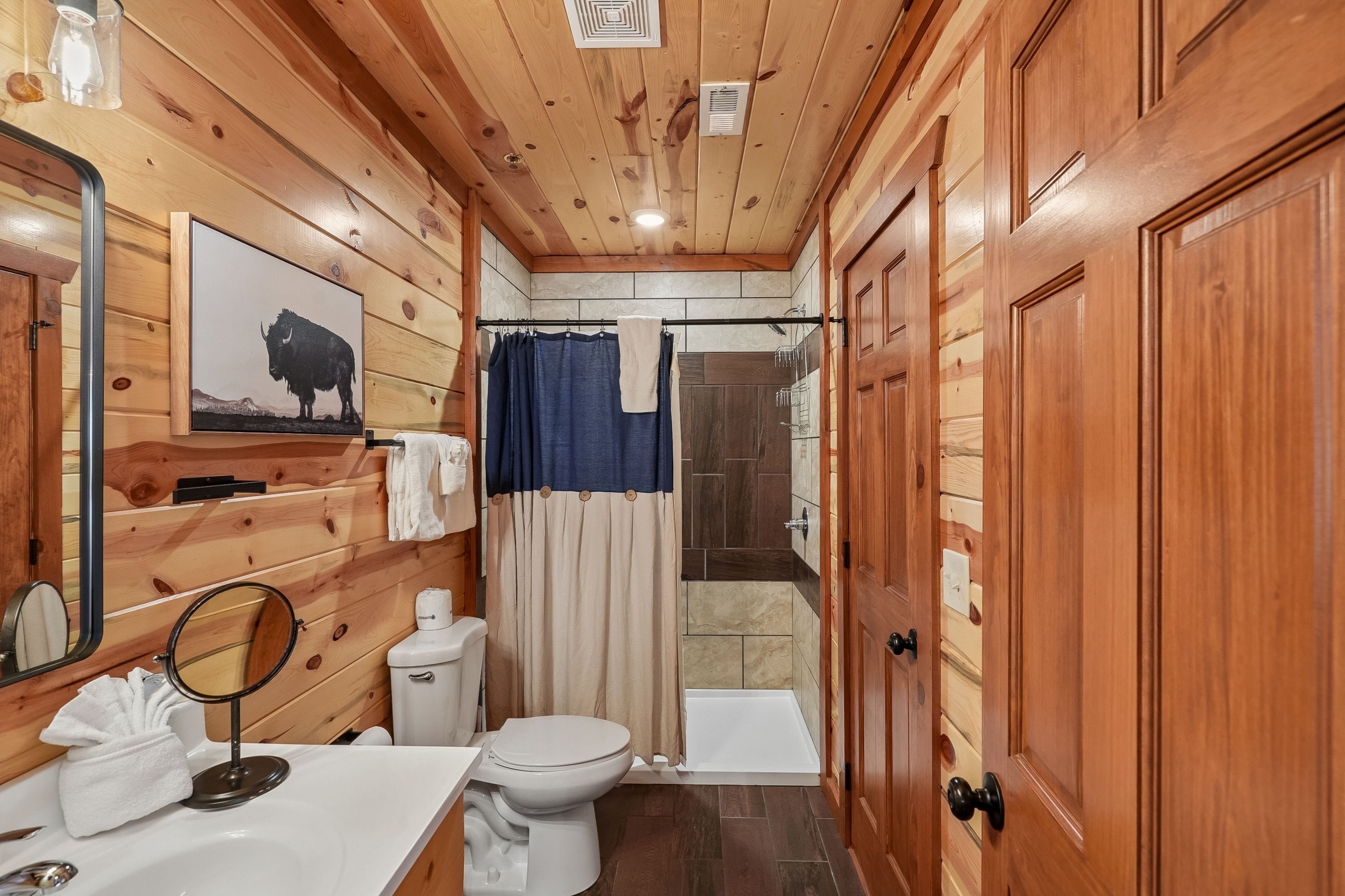 A bathroom with wooden walls, a toilet, a sink, a mirror, a shower curtain, and a door.